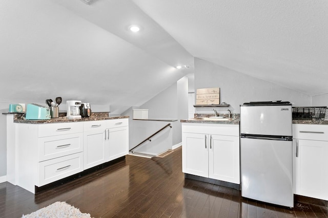 kitchen with refrigerator, lofted ceiling, dark stone counters, white cabinets, and dark hardwood / wood-style floors