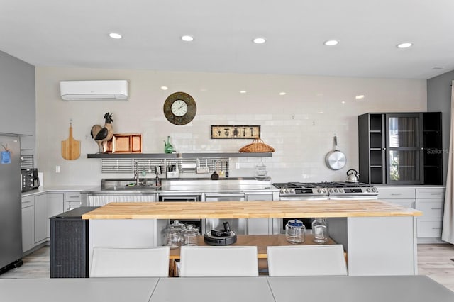 kitchen with a wall mounted AC, light hardwood / wood-style flooring, gray cabinetry, and wood counters