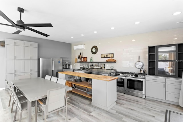 kitchen featuring appliances with stainless steel finishes, an AC wall unit, wooden counters, light hardwood / wood-style floors, and tasteful backsplash