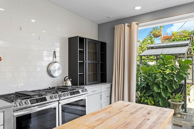 kitchen featuring tasteful backsplash, white cabinetry, butcher block counters, and stainless steel gas range oven