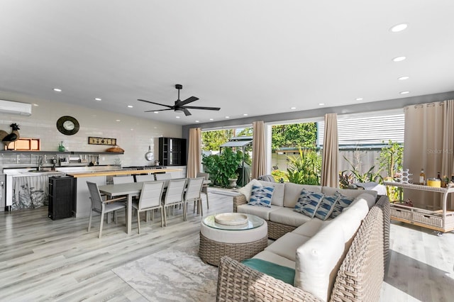 living room featuring sink, a wall mounted air conditioner, ceiling fan, and light hardwood / wood-style flooring