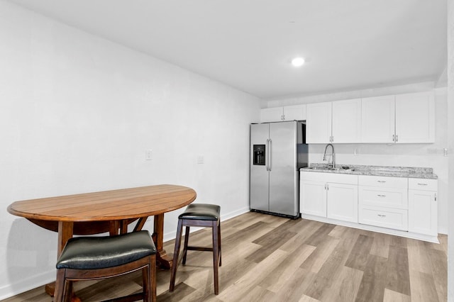 kitchen featuring white cabinets, sink, stainless steel refrigerator with ice dispenser, and light stone countertops