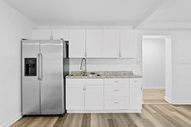 kitchen with sink, white cabinets, light stone countertops, and stainless steel fridge