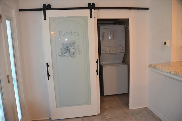 laundry area with light tile patterned floors, stacked washer and clothes dryer, and a barn door