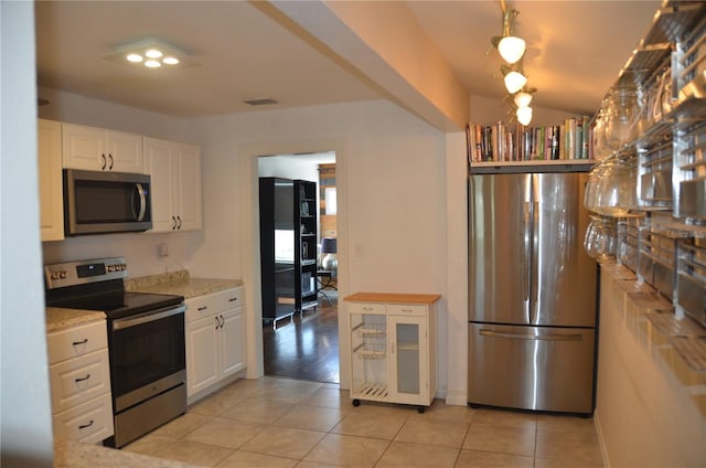 kitchen featuring appliances with stainless steel finishes, white cabinets, light tile patterned flooring, and light stone counters