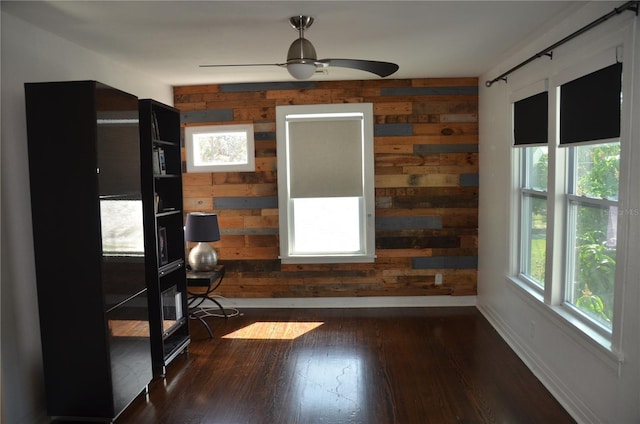 empty room with ceiling fan, wooden walls, and dark hardwood / wood-style floors