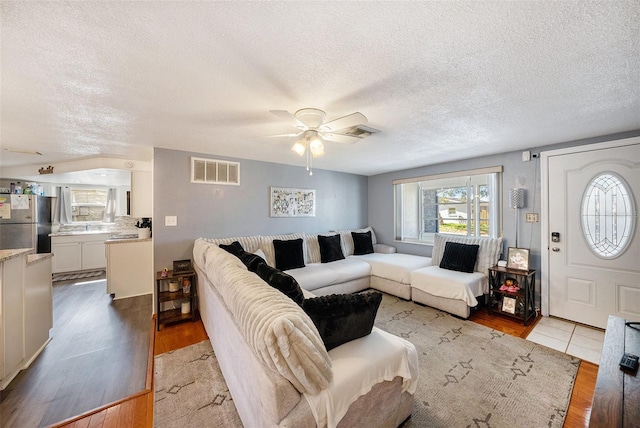 living room featuring ceiling fan, a textured ceiling, and light wood-type flooring