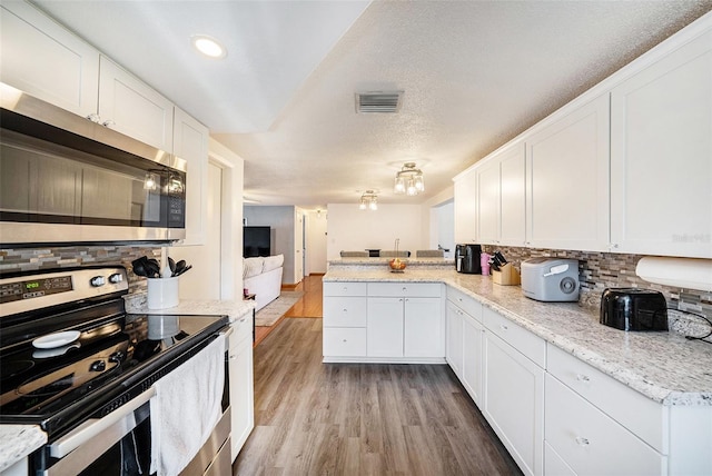 kitchen with light hardwood / wood-style flooring, stainless steel appliances, kitchen peninsula, and white cabinets