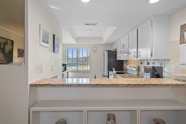 kitchen with a tray ceiling, visible vents, electric range oven, freestanding refrigerator, and white cabinetry