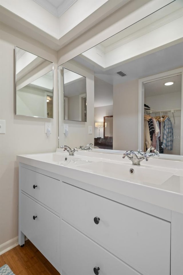 full bath with a walk in closet, double vanity, visible vents, a sink, and wood finished floors