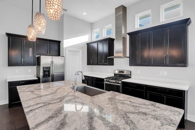 kitchen with a sink, appliances with stainless steel finishes, dark wood-style floors, wall chimney exhaust hood, and decorative light fixtures