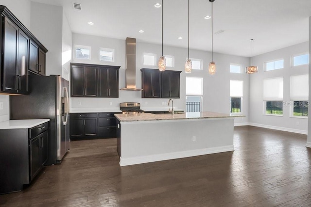 kitchen with a kitchen island with sink, stainless steel appliances, visible vents, hanging light fixtures, and wall chimney exhaust hood