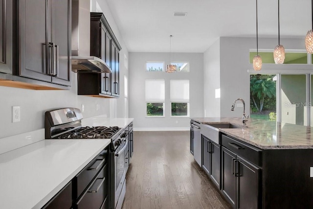 kitchen with stainless steel appliances, a sink, hanging light fixtures, wall chimney exhaust hood, and a center island with sink