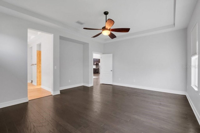 empty room with a raised ceiling, dark wood finished floors, visible vents, and baseboards