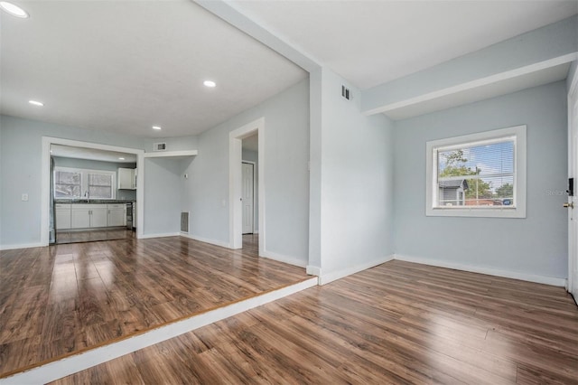 unfurnished living room featuring visible vents, baseboards, and wood finished floors