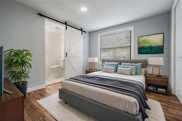 bedroom with a barn door, visible vents, dark wood finished floors, and baseboards