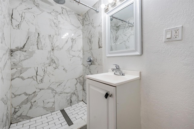 full bath with a textured wall, vanity, and a marble finish shower