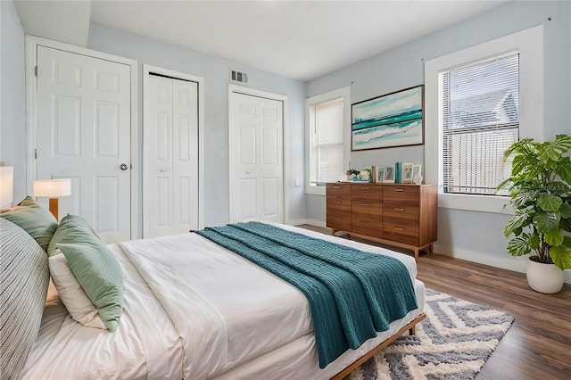 bedroom featuring multiple closets, visible vents, baseboards, and wood finished floors