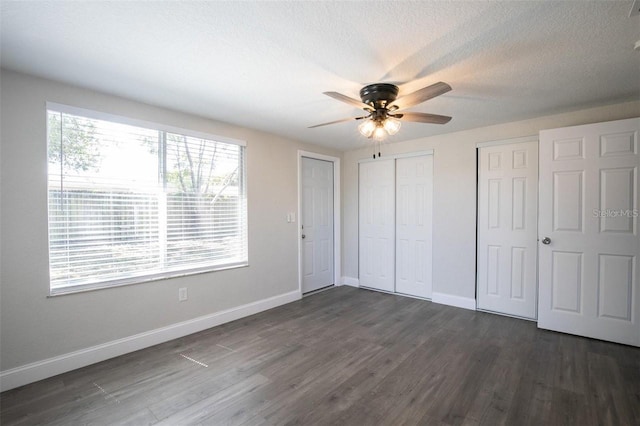 unfurnished bedroom featuring multiple closets, ceiling fan, dark wood-type flooring, and a textured ceiling