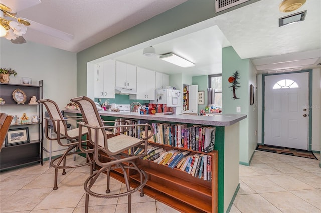 kitchen with sink, light tile patterned floors, kitchen peninsula, ceiling fan, and white cabinets