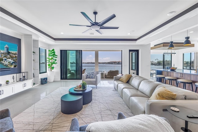 living room featuring ceiling fan, a water view, a tray ceiling, and built in features