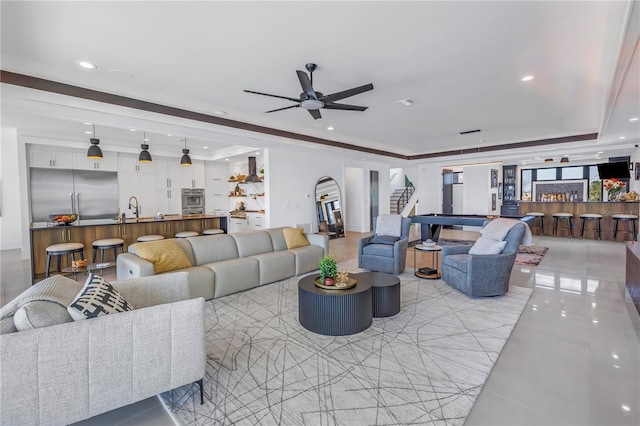 living room featuring a raised ceiling, indoor wet bar, light tile patterned floors, and ceiling fan