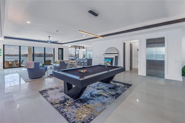 game room with a water view, elevator, a tray ceiling, ceiling fan, and billiards