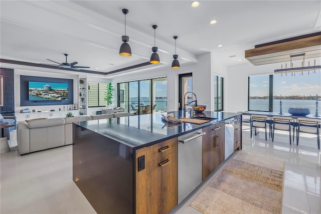 kitchen with a center island with sink, decorative light fixtures, a water view, sink, and dishwasher