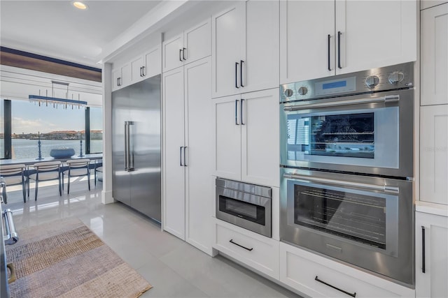 kitchen featuring white cabinets, built in appliances, light tile patterned floors, and a water view