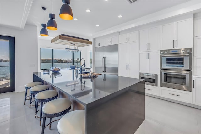 kitchen featuring a center island with sink, a water view, appliances with stainless steel finishes, and pendant lighting