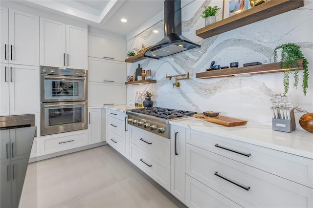 kitchen featuring island range hood, white cabinetry, light stone counters, and appliances with stainless steel finishes