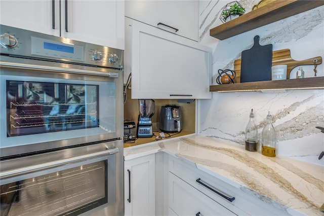 kitchen featuring double oven, tasteful backsplash, light stone counters, and white cabinets