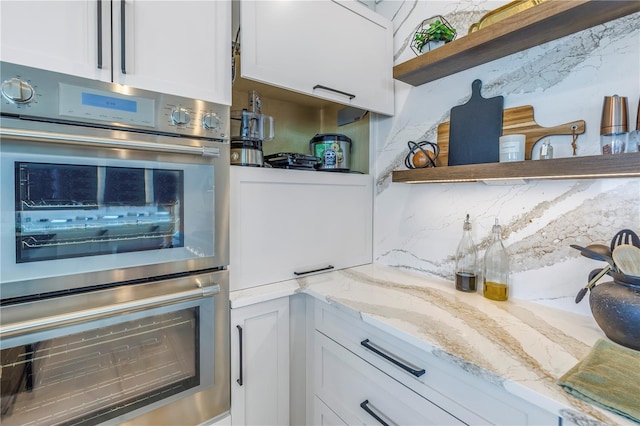 kitchen with white cabinetry, stainless steel double oven, light stone countertops, and tasteful backsplash