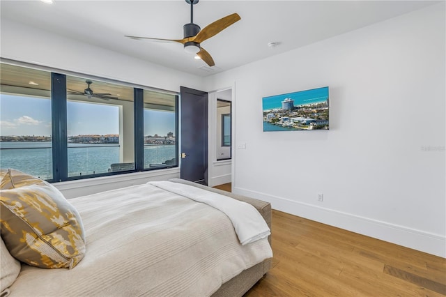 bedroom with hardwood / wood-style flooring, a water view, and ceiling fan