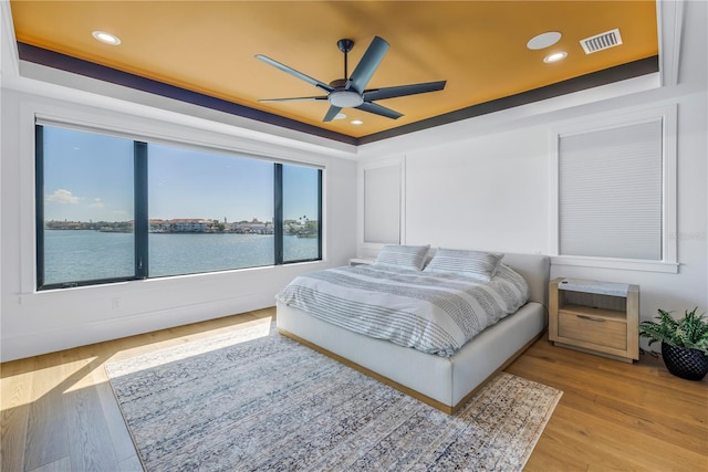 bedroom with a water view, a raised ceiling, and light hardwood / wood-style flooring