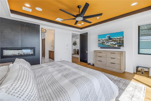 bedroom with a fireplace, light hardwood / wood-style flooring, ceiling fan, and a raised ceiling