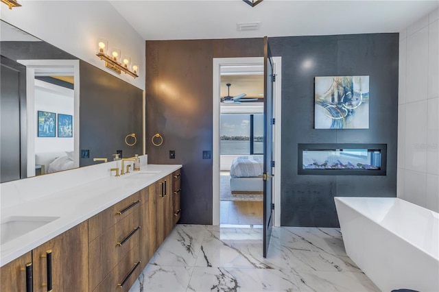 bathroom with a multi sided fireplace, ceiling fan, a bathtub, and vanity