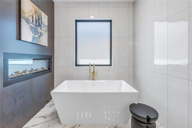 bathroom with a wealth of natural light, a bathtub, and tile walls