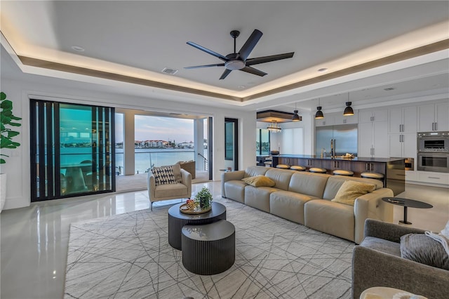 living room with a water view, ceiling fan, and a raised ceiling