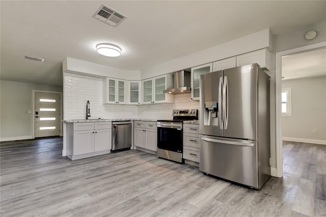 kitchen with a sink, visible vents, appliances with stainless steel finishes, wall chimney range hood, and backsplash