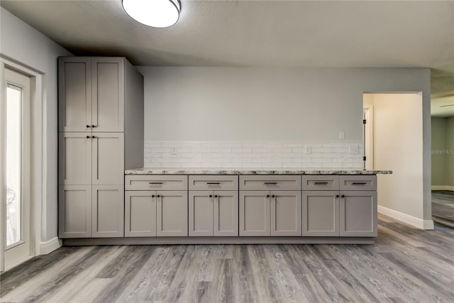 kitchen with light wood-type flooring, backsplash, baseboards, and light stone countertops