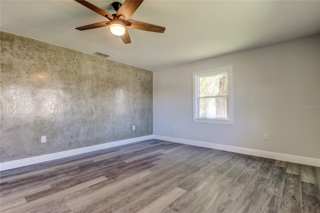 spare room with a ceiling fan, dark wood finished floors, visible vents, and baseboards