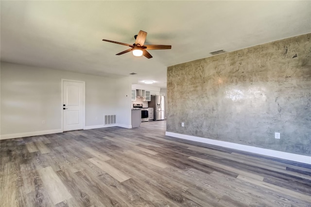 unfurnished living room with ceiling fan, wood finished floors, visible vents, and baseboards