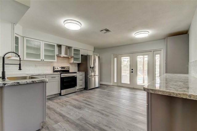 kitchen featuring visible vents, wall chimney exhaust hood, appliances with stainless steel finishes, french doors, and a sink