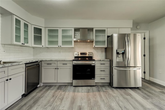 kitchen with stainless steel appliances, tasteful backsplash, wall chimney exhaust hood, and light wood-style floors