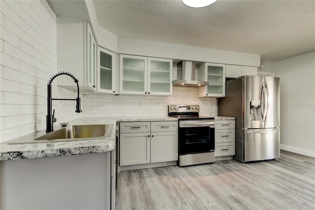 kitchen with light wood-style flooring, a sink, appliances with stainless steel finishes, wall chimney range hood, and decorative backsplash