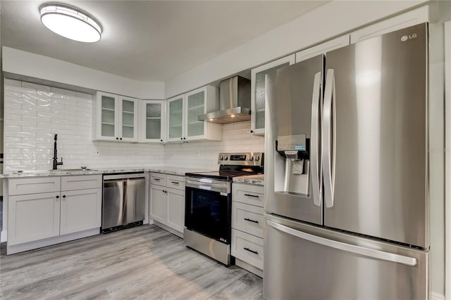 kitchen featuring light stone counters, a sink, appliances with stainless steel finishes, wall chimney exhaust hood, and tasteful backsplash