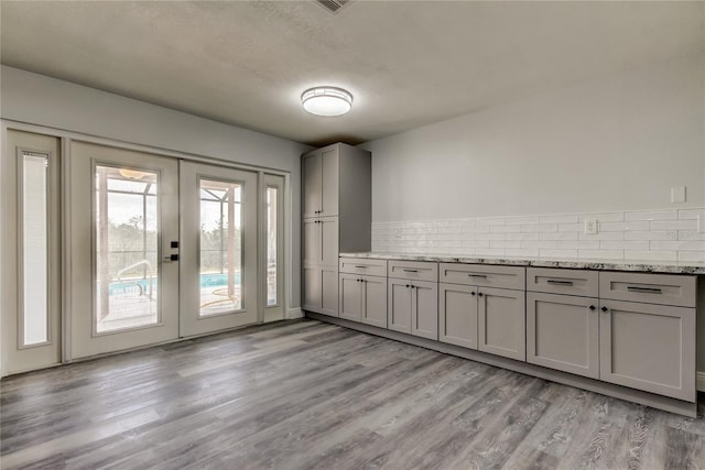 kitchen with decorative backsplash, french doors, light stone countertops, gray cabinetry, and light wood-style floors