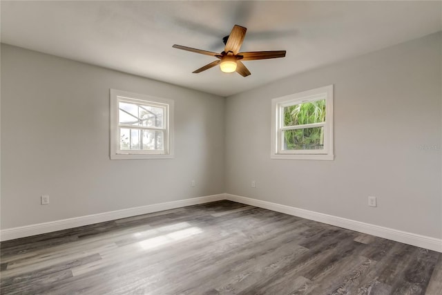 spare room with dark wood-type flooring, a healthy amount of sunlight, ceiling fan, and baseboards