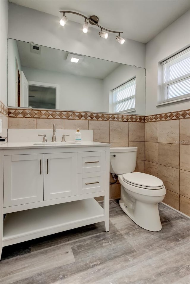 bathroom featuring vanity, wood finished floors, toilet, and tile walls